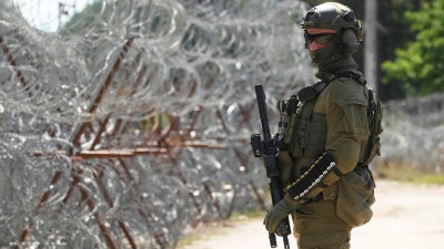 A Polish border guard stands near a barbed wire fence at the Polish-Belarusian border in Polowce, Poland, July 21, 2025. © 2025 AP Photo/Czarek Sokolowski