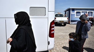 Migrants walk towards a bus to be taken for processing after disembarking from a Royal National Lifeboat Institution (RNLI) lifeboat on a beach after crossing the English Channel, in Dungeness, England, on June 15, 2022.