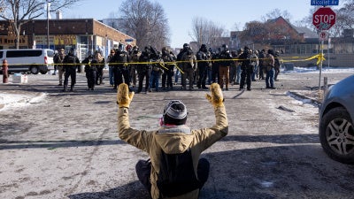Un manifestant assis levait les bras face à des agents fédéraux de l’ICE et à des policiers dans une rue de Minneapolis, au Minnesota, non loin du lieu ou Alex Pretti, un citoyen américain a été mortellement blessé par des tirs d'agents fédéraux dans la matinée du samedi 24 janvier 2026.