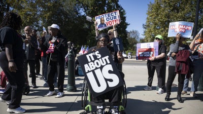 A man in a wheelchair holds a protest sign at a demonstration