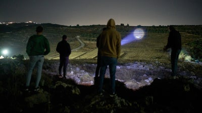 A Palestinian uses a flashlight on a nearby hill while taking part in a night watch with other volunteers to deter settler attacks on the West Bank village of Sinjil, July 16, 2026.