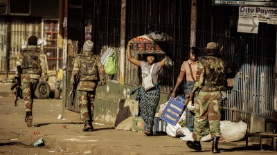 A vendor seeks cover as soldiers disperse demonstrators in Harare, Zimbabwe, after protests erupted over alleged fraud in the country's election on August 1, 2018.