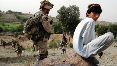 An Afghan boy watches as US Army 101st Airborne soldiers move in during a mission in southeastern Afghanistan, July 23, 2002. 