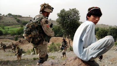 An Afghan boy watches as US Army 101st Airborne soldiers move in during a mission in southeastern Afghanistan, July 23, 2002. 