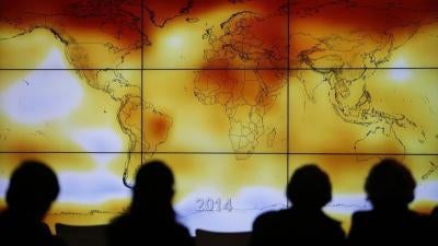 Participants are seen in silhouette as they look at a screen showing a world map with climate anomalies during the World Climate Change Conference 2015 (COP21).
