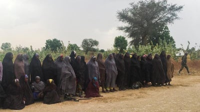 A man carrying a Boko Haram flag walks past a group of 82 Chibok girls, who were held captive for three years by Islamist militants, as the girls wait to be released in exchange for several militant commanders, near Kumshe, Nigeria May 6, 2017.