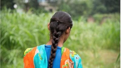 A young girl with long hair portraid from behind, in front of a field. 
