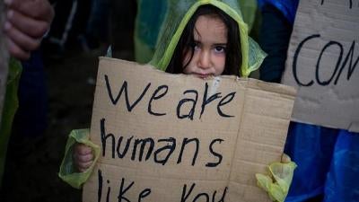  Une fillette tient une pancarte lors d'une manifestation de migrants et de réfugiés bloqués dans un camp provisoire près du village d’Idomeni, en Grèce, le 23 mars 2016.