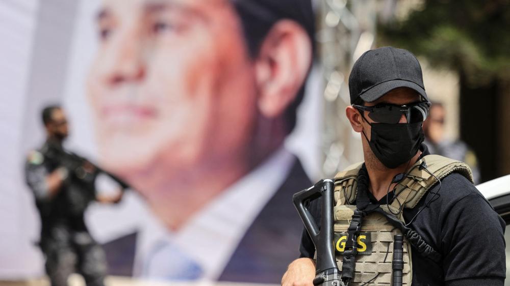 An Egyptian intelligence security detail member stands guard near a banner showing President Abdel Fattah al-Sisi.