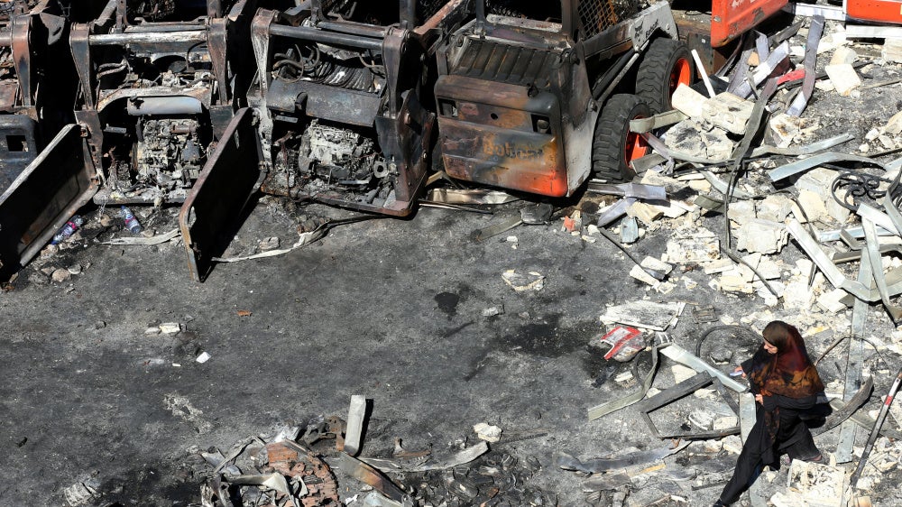 A woman walks in front of charred agricultural equipment, at the site of an Israeli strike in the southern Lebanese village of Msayleh, on October 11, 2025. 