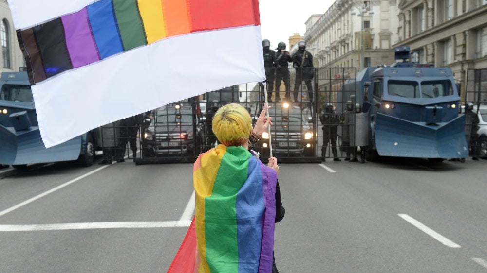 An activist waves a rainbow flag in front of a line of police