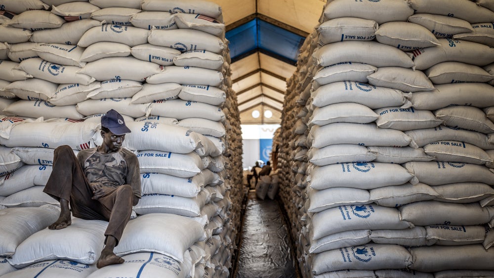 A worker sits atop sacks of food aid in a hangar where supplies are piling up because deliveries have halted because of the conflict at a World Food Programme (WFP) warehouse in Bor, Jonglei State, on February 13, 2026.