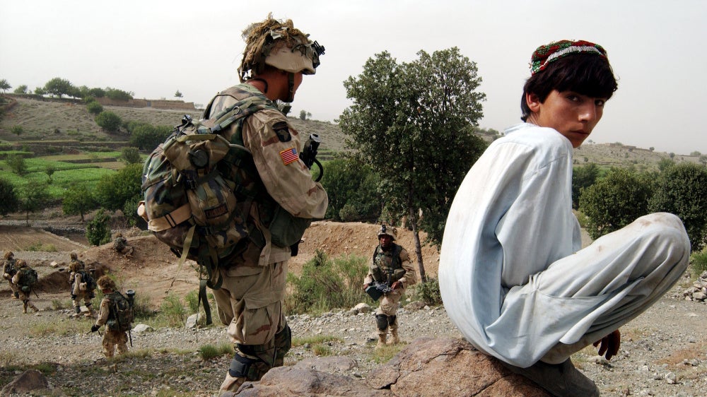 An Afghan boy watches as US Army 101st Airborne soldiers move in during a mission in southeastern Afghanistan, July 23, 2002. 