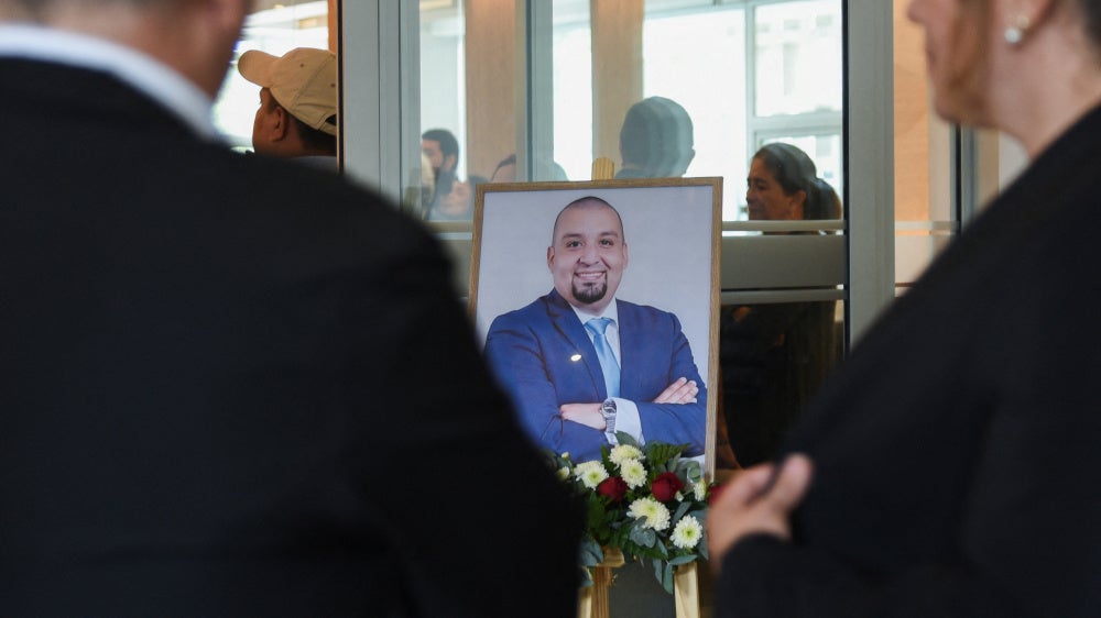 People stand near a framed photo of Guatemalan lawyer and anti-corruption figure Juan Francisco Solorzano Foppa, who died after being shot by unknown assailants on Saturday while visiting a sports center, during his wake at a funeral home in Guatemala City, Guatemala, October 19, 2026.