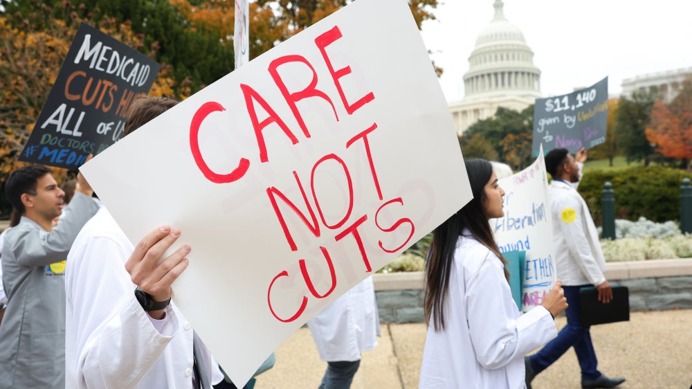Protesters hold a placard that reads "Care Not Cuts"