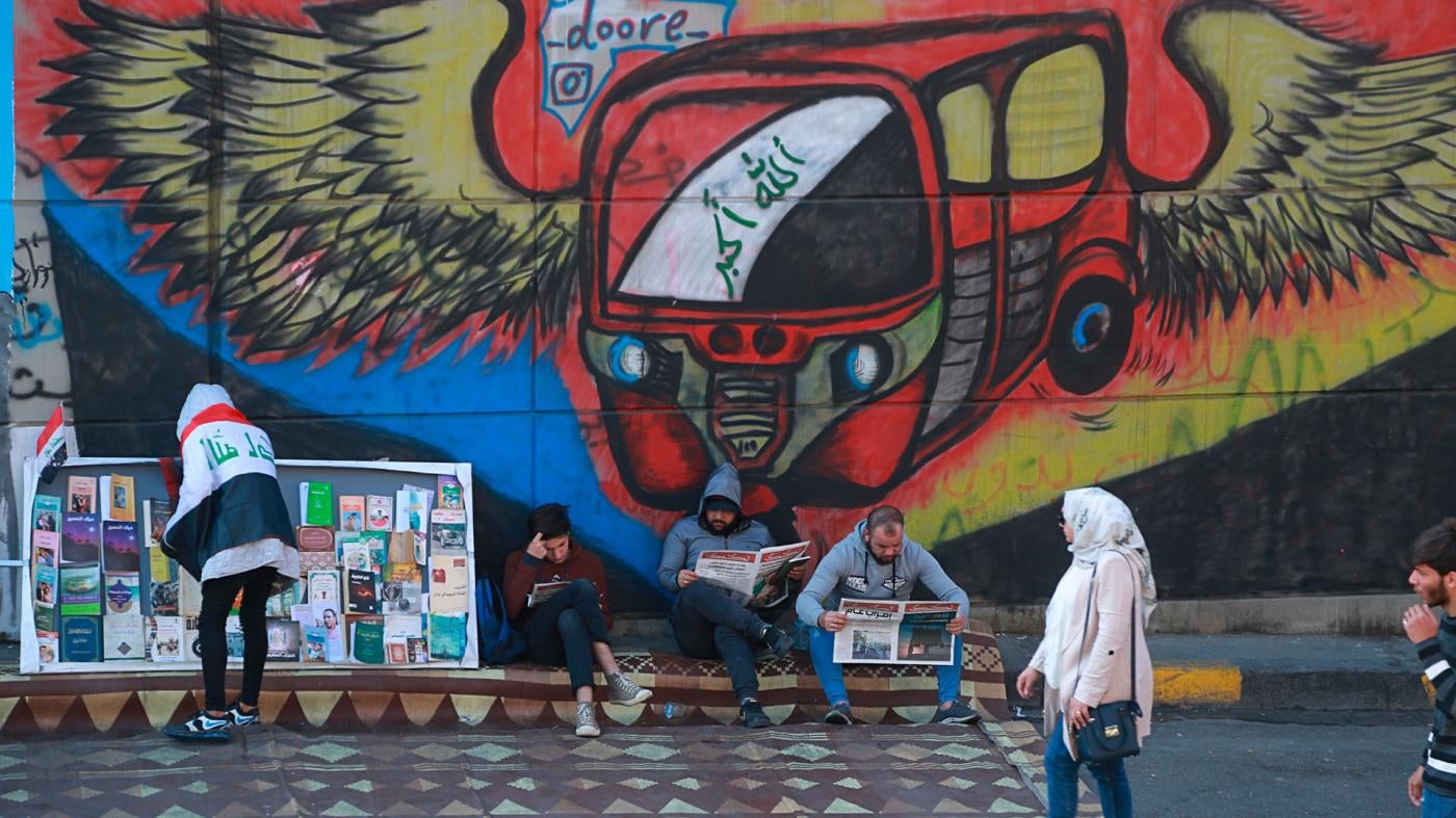 Protesters read copies of newspapers in front of graffiti in Tahrir Square, Baghdad, Iraq, November 20, 2019.