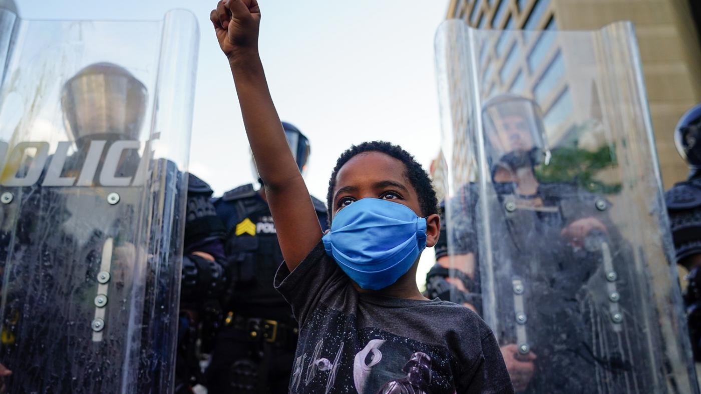 Child raises fist in front of line of police