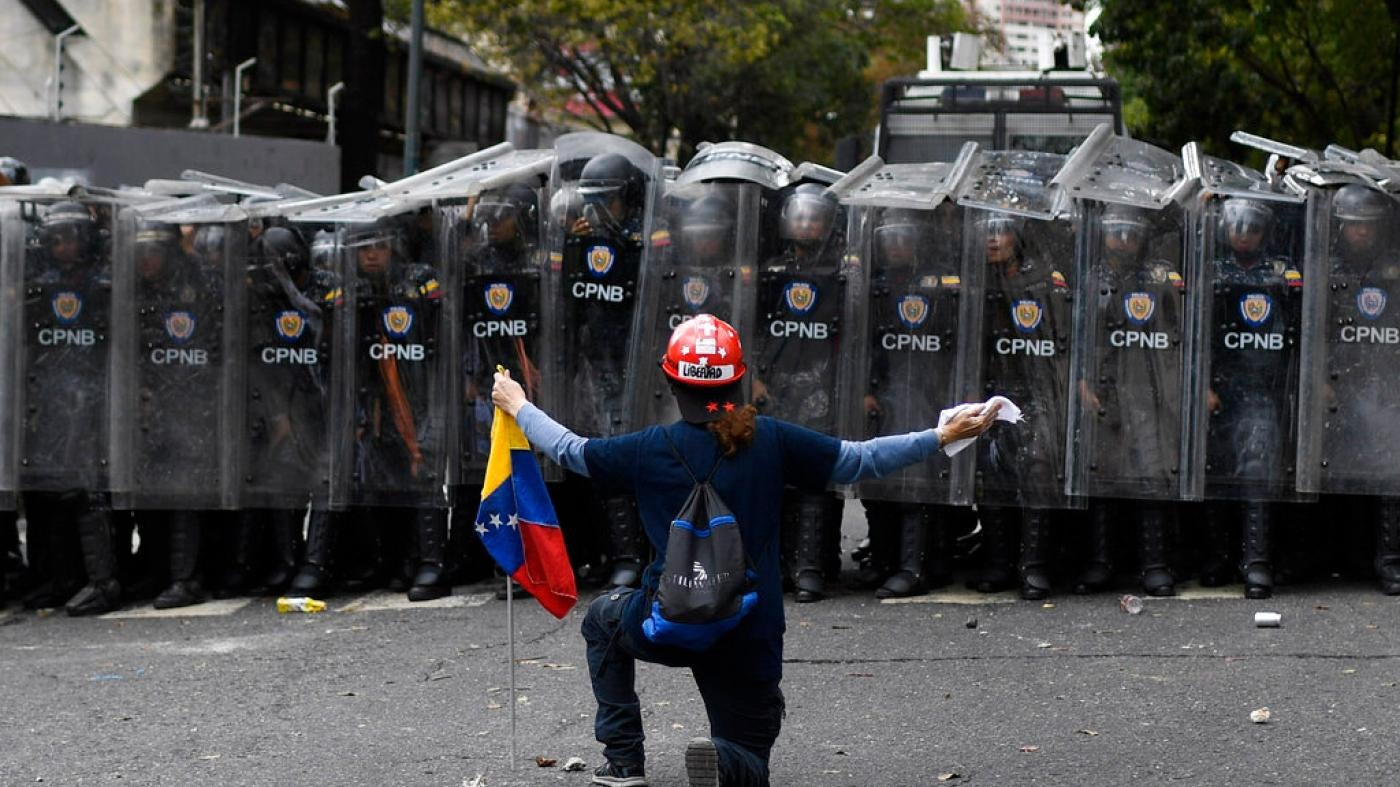 A man kneels in front of police blocking a march called by opposition political leader Juan Guaido in Caracas, Venezuela, Tuesday, March 10, 2020. 