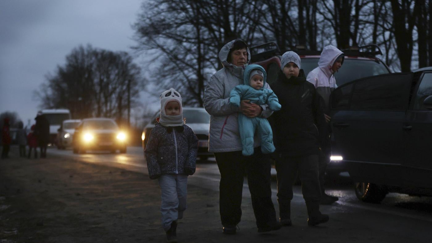 A family walks alongside a road at night with their belongings