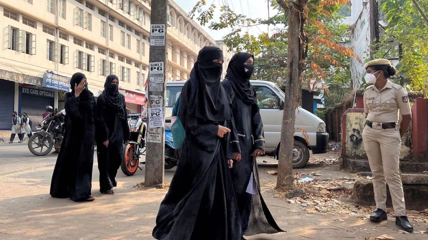  印度南部卡納塔克（Karnataka）邦宣布禁止全身罩袍（hijab）後，烏都比（Udupi）一所公立學校女生身穿罩袍到校上課，從守衛校門的女警員眼前走過，2022年2月16日。
 © 2022 Sunil Kataria/REUTERS
