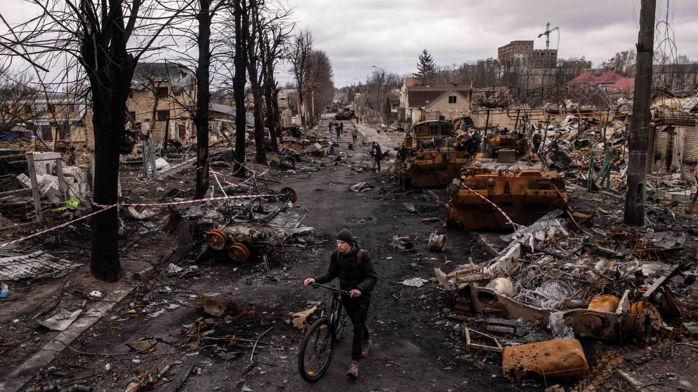  男子推腳踏車走過斷垣殘壁和被毀的俄羅斯軍用車輛，烏克蘭，布查（Bucha），2022年4月6日。據人權觀察記錄，俄軍在2022年3月12至31日佔領基輔西北方城鎮布查期間，顯然犯下許多戰爭罪行。
 © 2022 Chris McGrath/Getty Images 