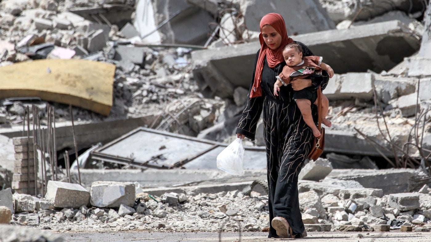 A woman carries a toddler across a field of rubble