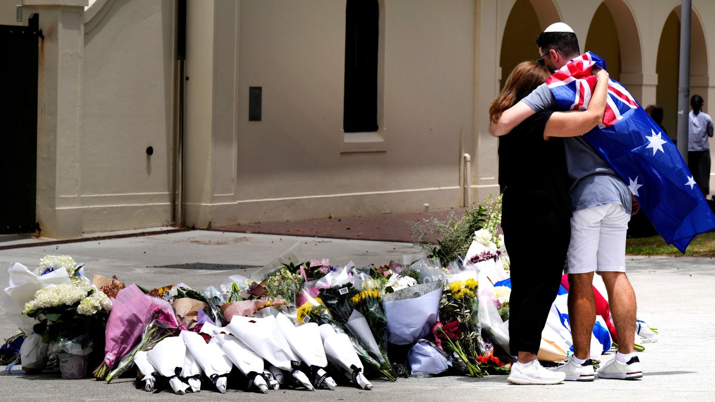Un homme et une femme s’étreignaient devant le pavillon de Bondi, le 15 décembre 2025, près de nombreux bouquets de fleurs déposés en hommage aux victimes de l’attentat perpétré la veille contre une la foule de personnes qui célébraient la fête juive de Hanouka sur la plage de Bondi, à l’est de Sydney, en Australie.