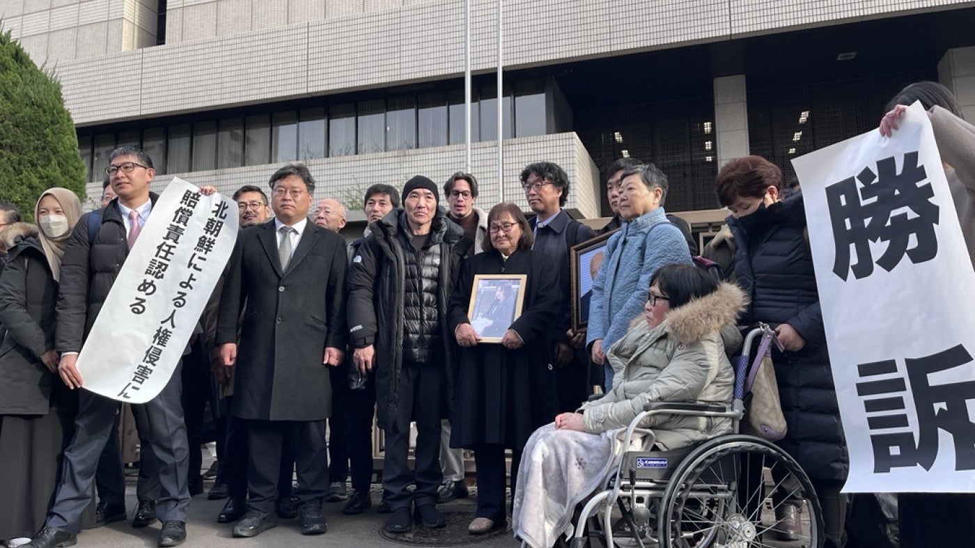 Plaintiffs holding flags declaring the verdict in front of the Tokyo district court main gate, January 26, 2026. 