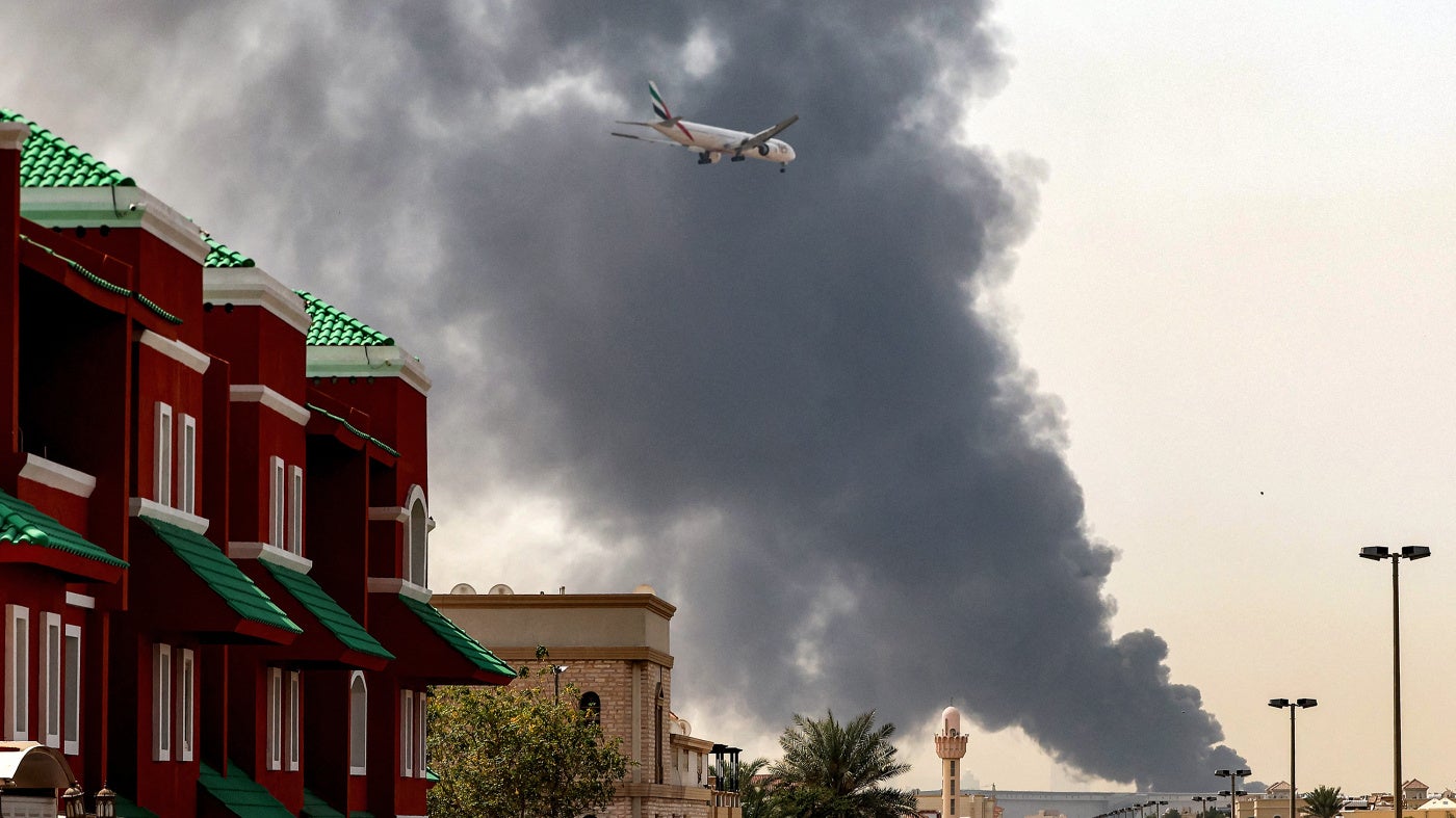 An Emirates aircraft prepares for landing as a smoke plume rises from an ongoing fire near Dubai International Airport, UAE, on March 16, 2026. 