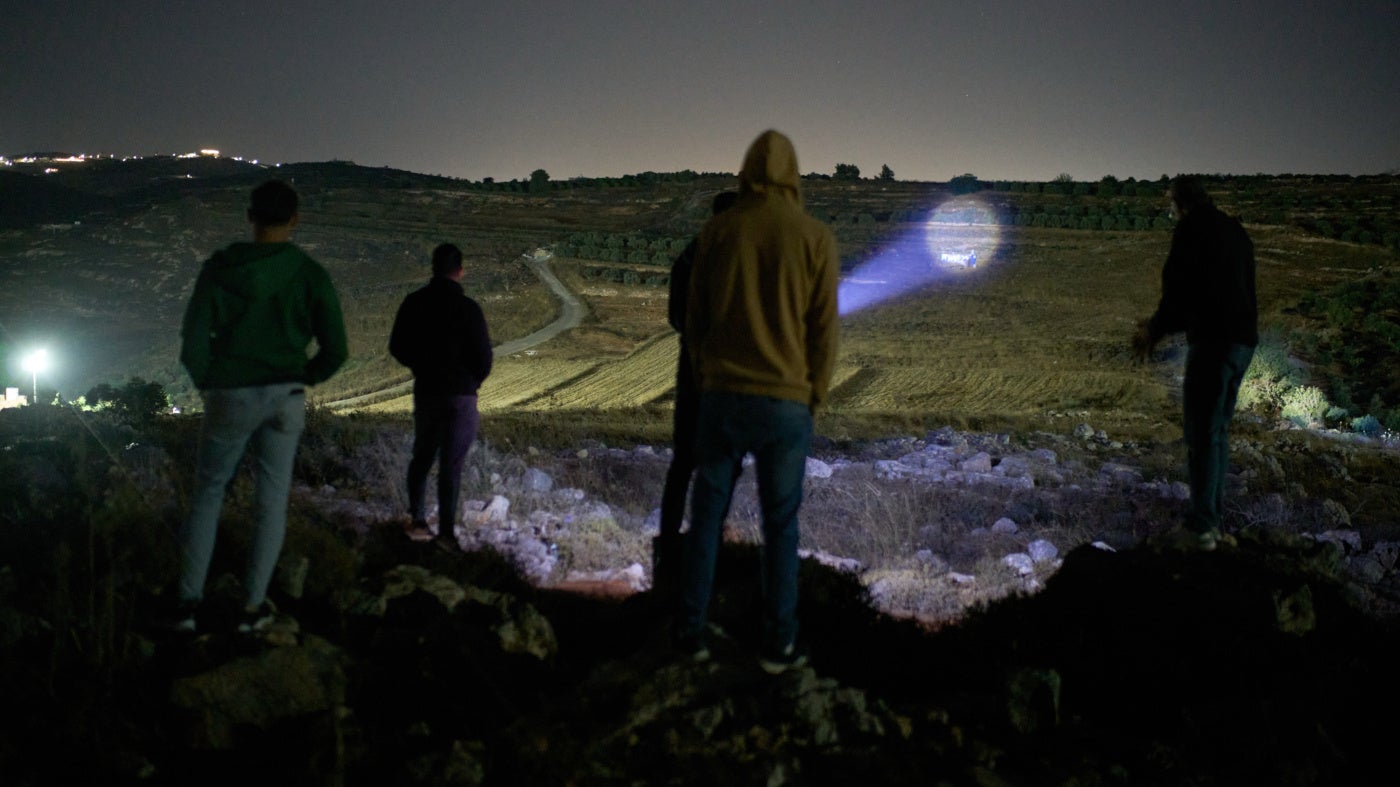 A Palestinian uses a flashlight on a nearby hill while taking part in a night watch with other volunteers to deter settler attacks on the West Bank village of Sinjil, July 16, 2026.