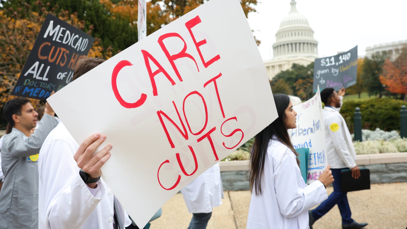 Protesters hold a placard that reads "Care Not Cuts"