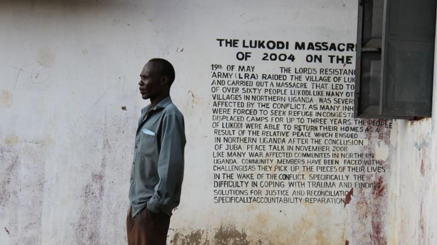 A community member in Lukodi stands next to a memorial of a May 19, 2004 massacre, one of the atrocities for which Dominic Ongwen is facing charges before the International Criminal Court. Over 4,000 victims are participating in the trial. 