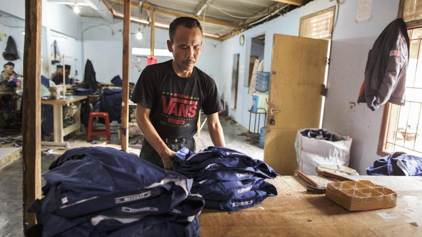 Man working in a clothing factory in Indonesia, stitching buttons 