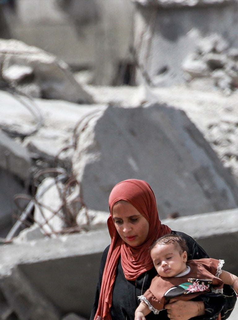 A woman carries a toddler across a field of rubble