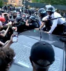 Police wave batons at a crowd atop a car