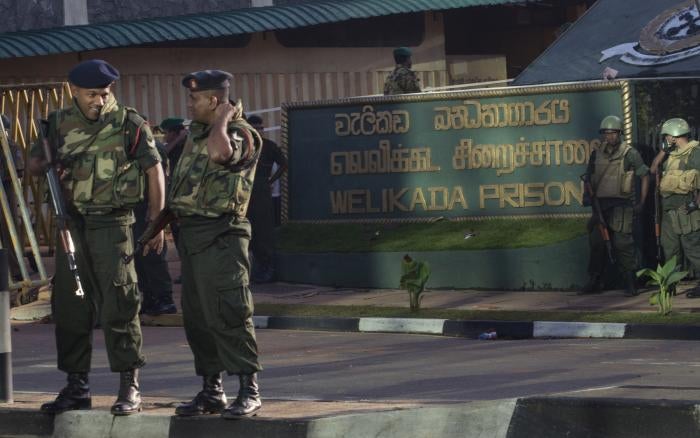Armed soldiers stand in front of a building with a sign that reads "Welikada Prison"
