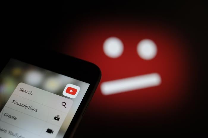 The YouTube video sharing application is seen on an iPhone with the symbol for unavailable content in the background in this photo illustration