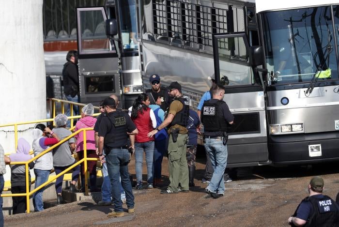 Uniformed police officers put people on a bus