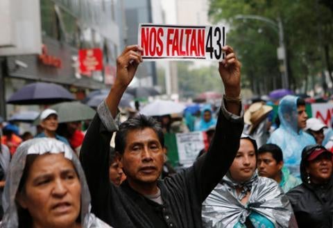 A protester holds up a sign next to relatives of some of the 43 missing students of Ayotzinapa College Raul Isidro Burgos during a march in Mexico City