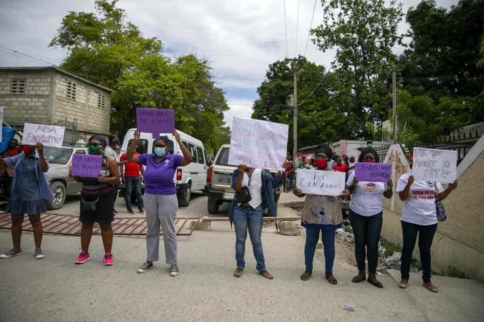 Women hold up signs demanding justice during the hearing of the president of the Fédération Haïtienne De Football (FHF), Yves Jean-Bart, regarding allegations that he abused female athletes at the country's national training center, outside the courthouse in Croix-des-Bouquets, Haiti, Thursday, May 14, 2020.