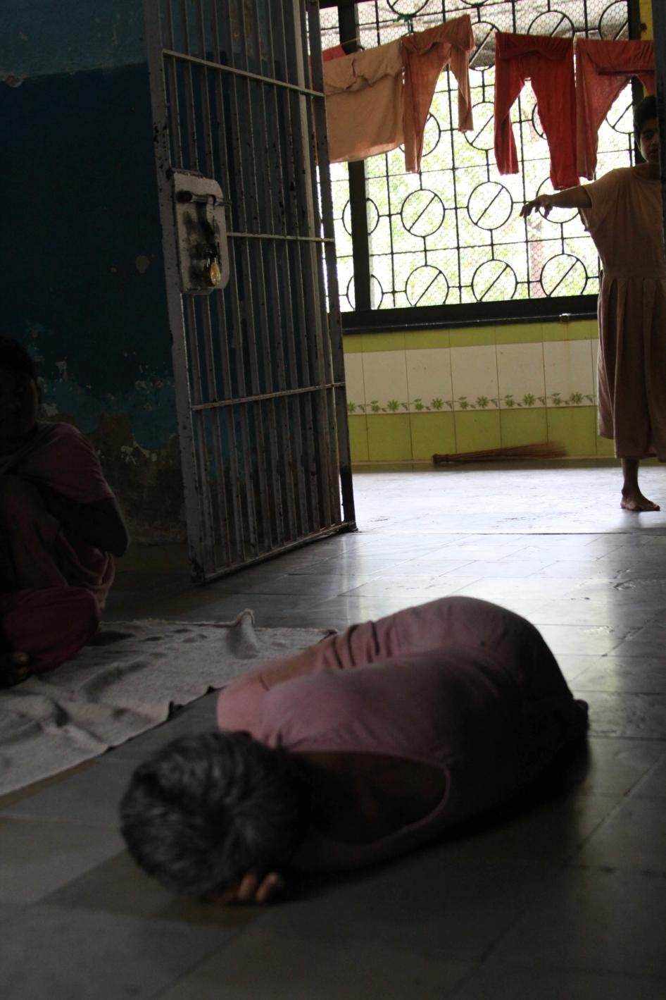 A woman in a pink dress lying on the floor of a room or cell.