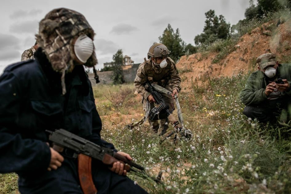 ثلاثة رجال بكامل معداتهم القتالية يرتدون كمامات واقية للوجه ضد فيروس كورونا، في طرابلس، ليبيا في 25 مارس/آذار 2020. 