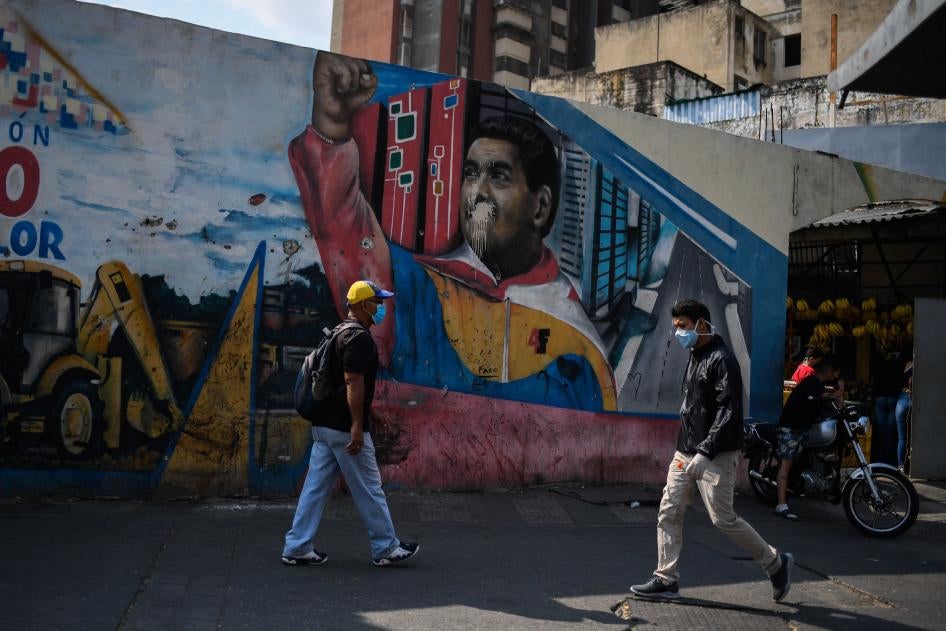 People wearing face masks walk past a mural depicting Venezuelan president Nicolas Maduro in Caracas on April 17, 2020, amid the novel coronavirus (COVID-19) outbreak. 