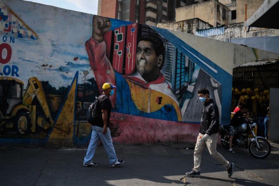 People wearing face masks walk past a mural depicting Venezuelan president Nicolas Maduro in Caracas on April 17, 2020, amid the novel coronavirus (COVID-19) outbreak