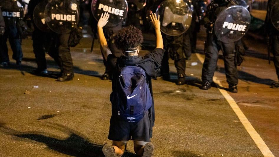 a protestor kneels in front of police