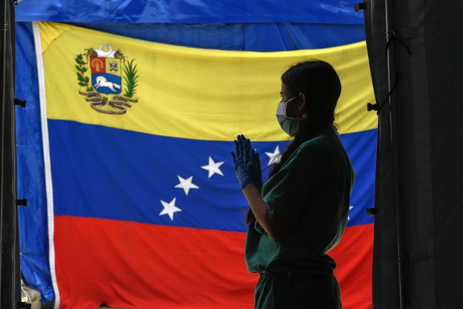 Un miembro de Médicos sin Fronteras espera a pacientes para realizarse tests de Covid-19 frente a una bandera venezolana en el Hospital Pérez de Leon en Petare, al este de Caracas, el 23 de junio de 2020, en el medio de la pandemia del coronavirus.