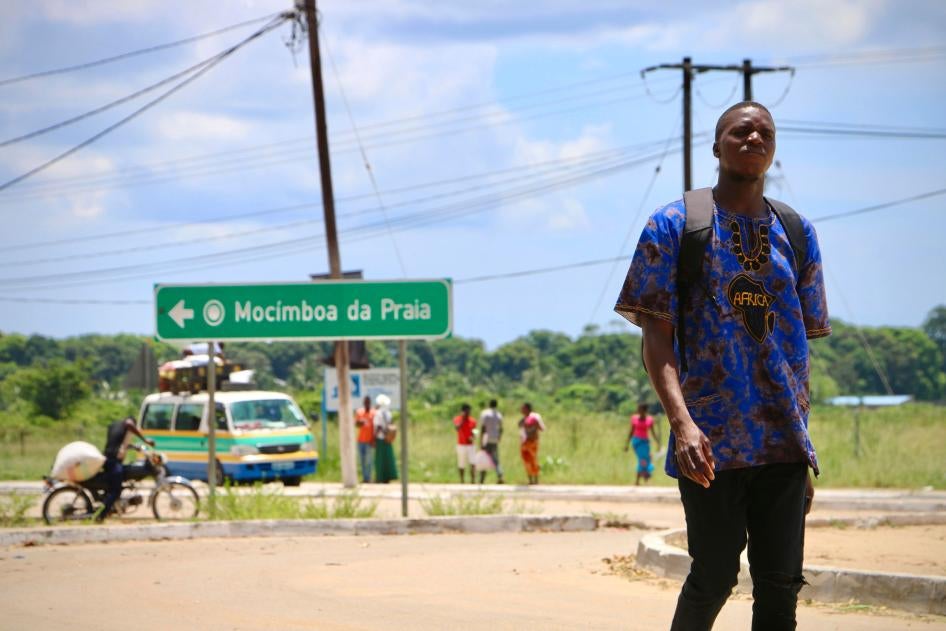 A man walks down a street with a sign for the town "Mocimboa da Praia" behind him