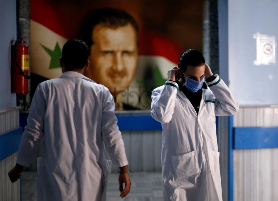 Deux membres du personnel médical marchaient dans le couloir d’un hôpital à Damas, le 19 mars 2020, devant un portrait géant du président syrien Bachar al-Assad. 