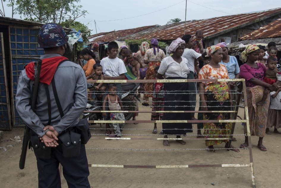 Un policier birman surveillait un groupe de musulmans rohingyas rassemblés derrière une clôture du camp de Thet Kae Pyin dans la zone de Sittwe (État de Rakhine), au Myanmar, le 7 septembre 2016. Des milliers de Rohingyas sont confinés dans des camps dans cette région, depuis 2012.