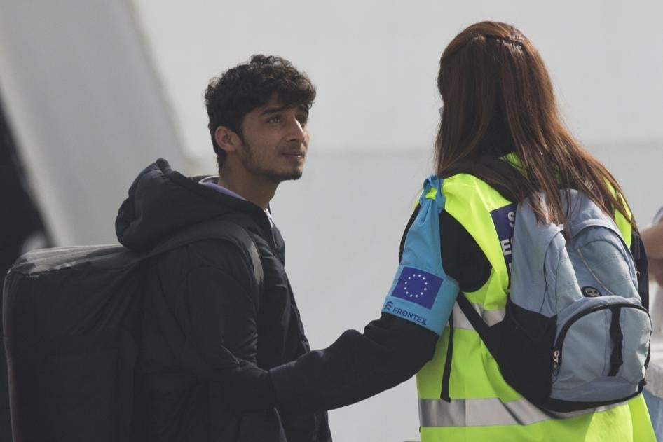 An officer from the European Union’s border protection agency, Frontex, holds the arm of a migrant as they board a ferry in the port of Mytilini, Lesbos island, Greece, on Friday, April 8, 2016.